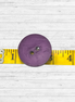 Purple button on a yellow measuring tape against a white wooden background