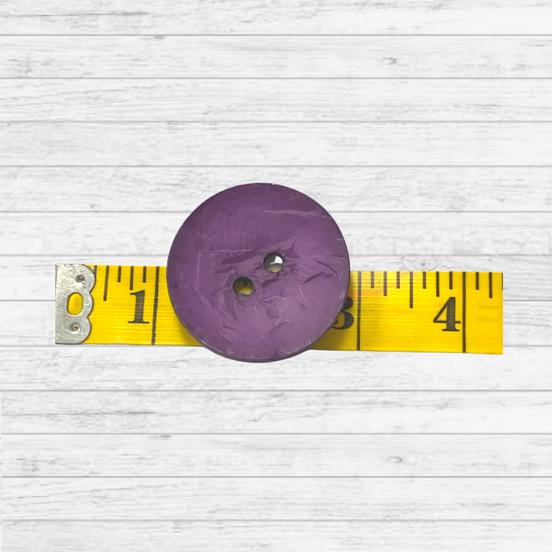 Purple button on a yellow measuring tape against a white wooden background