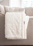 White textured blanket on a gray sofa with a blurred window background