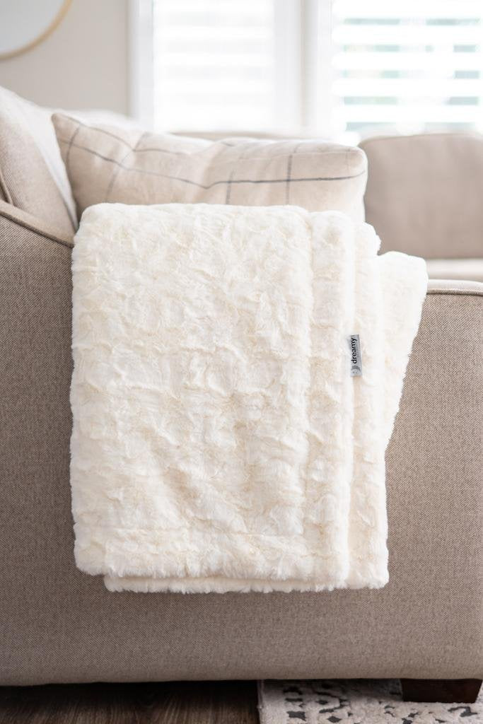White textured blanket on a gray sofa with a blurred window background