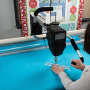 Person operating a quilting machine with a colorful quilt in the background