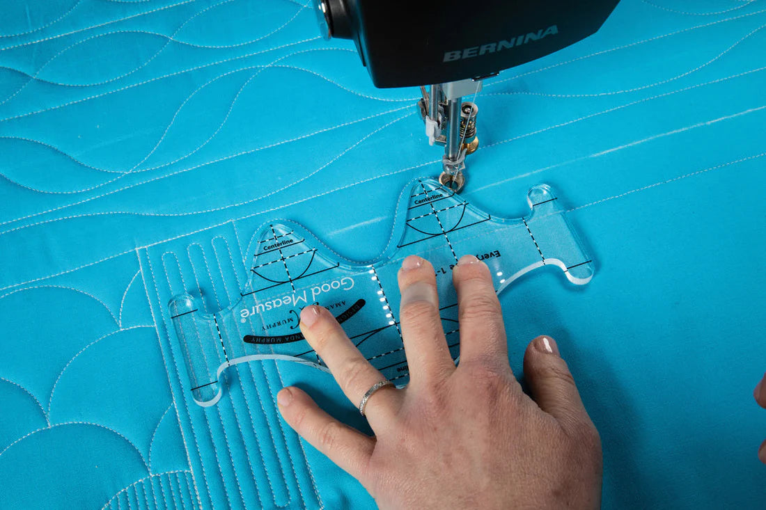 Sewing machine with a blue quilt and hand guiding a tool